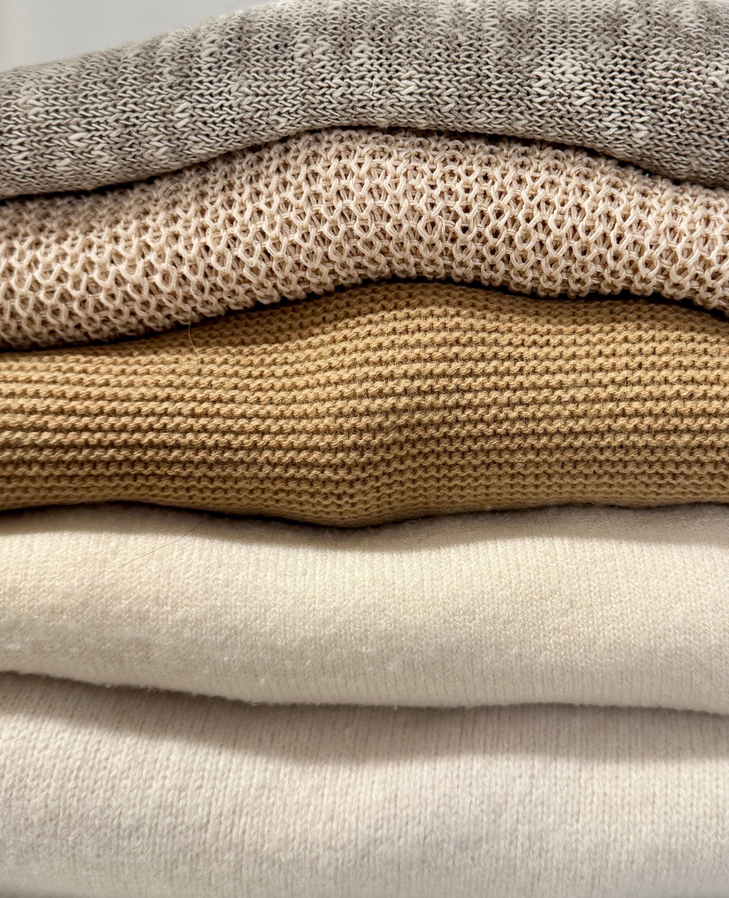 A close-up stack of folded sweaters in warm neutral tones